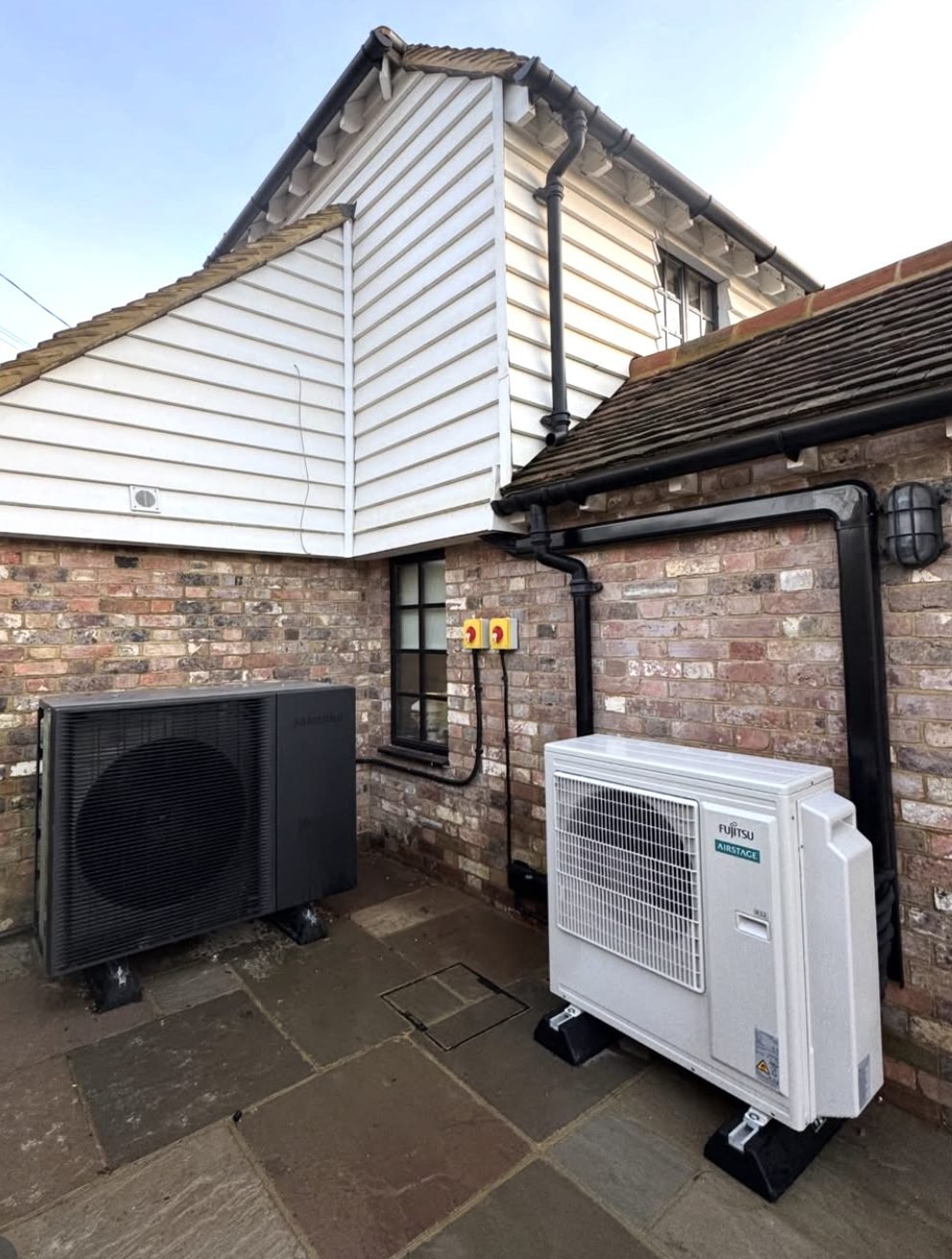 Two outdoor condenser units installed neatly on a patio with boxed pipework